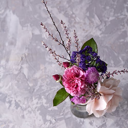 Glass vase containing pink garden roses, blue statice flowers, and foliage.