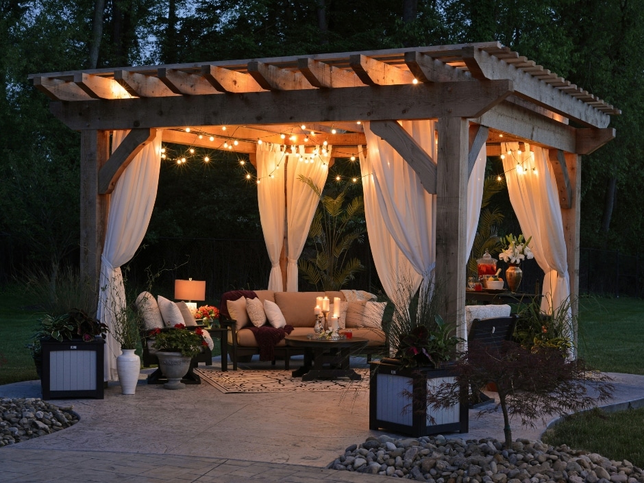 An outdoor living space at night featuring a pergola with string lights, comfortable seating, and decor.