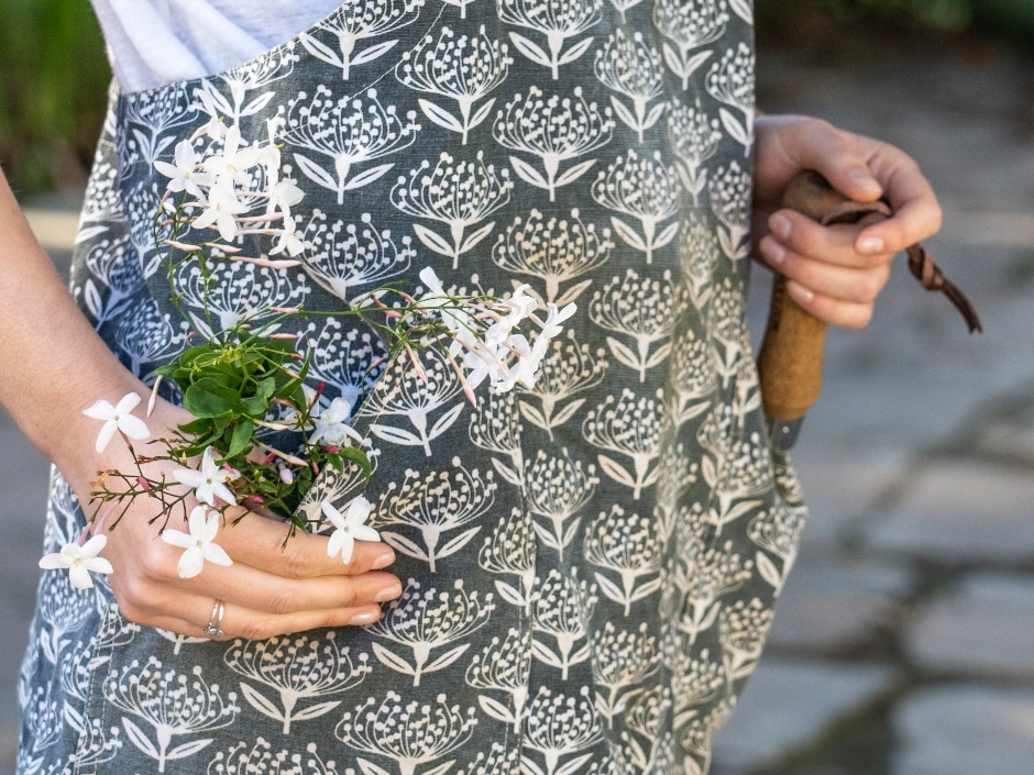 A person holds a bouquet of small white flowers against their patterned clothes, which feature a white floral design on grey fabric.