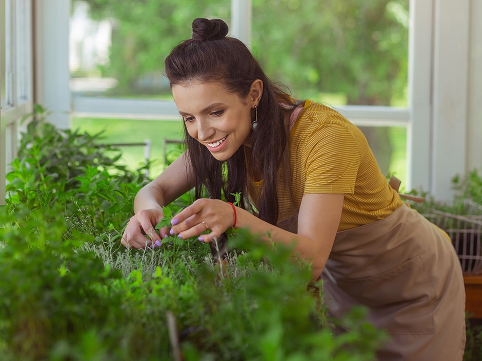 Woman in yellow top smiling while tending to potted herbs outdoors.