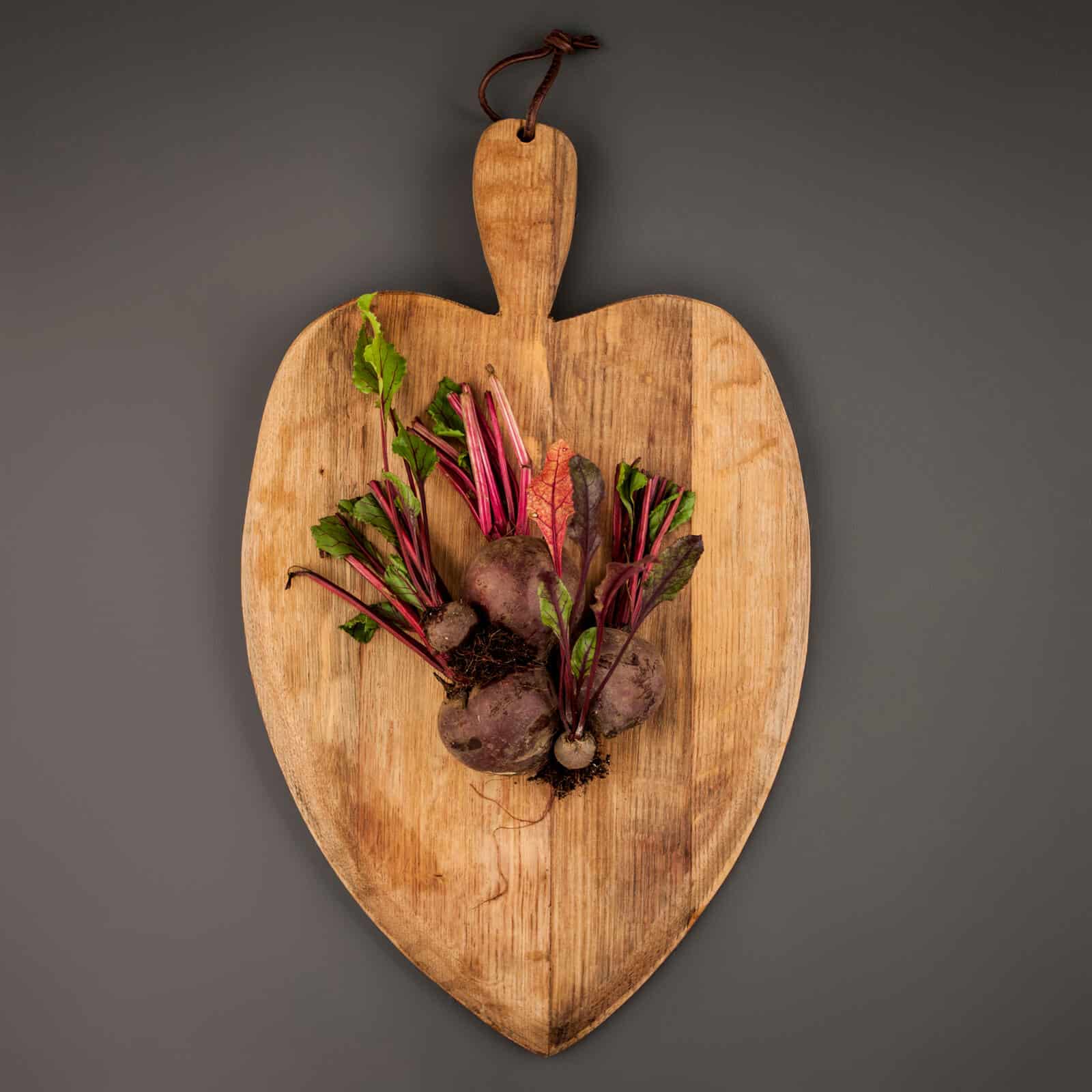 Wooden apple-shaped chopping board with beetroot leaves and roots.