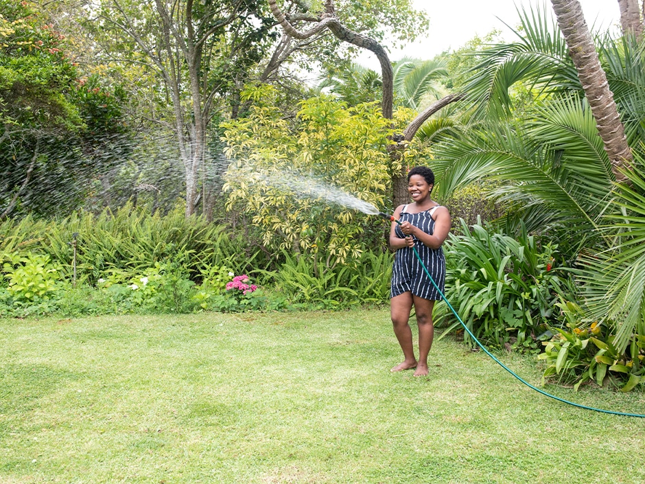 Person watering lawn with a hose-pipe sprinkler in a lush green garden.