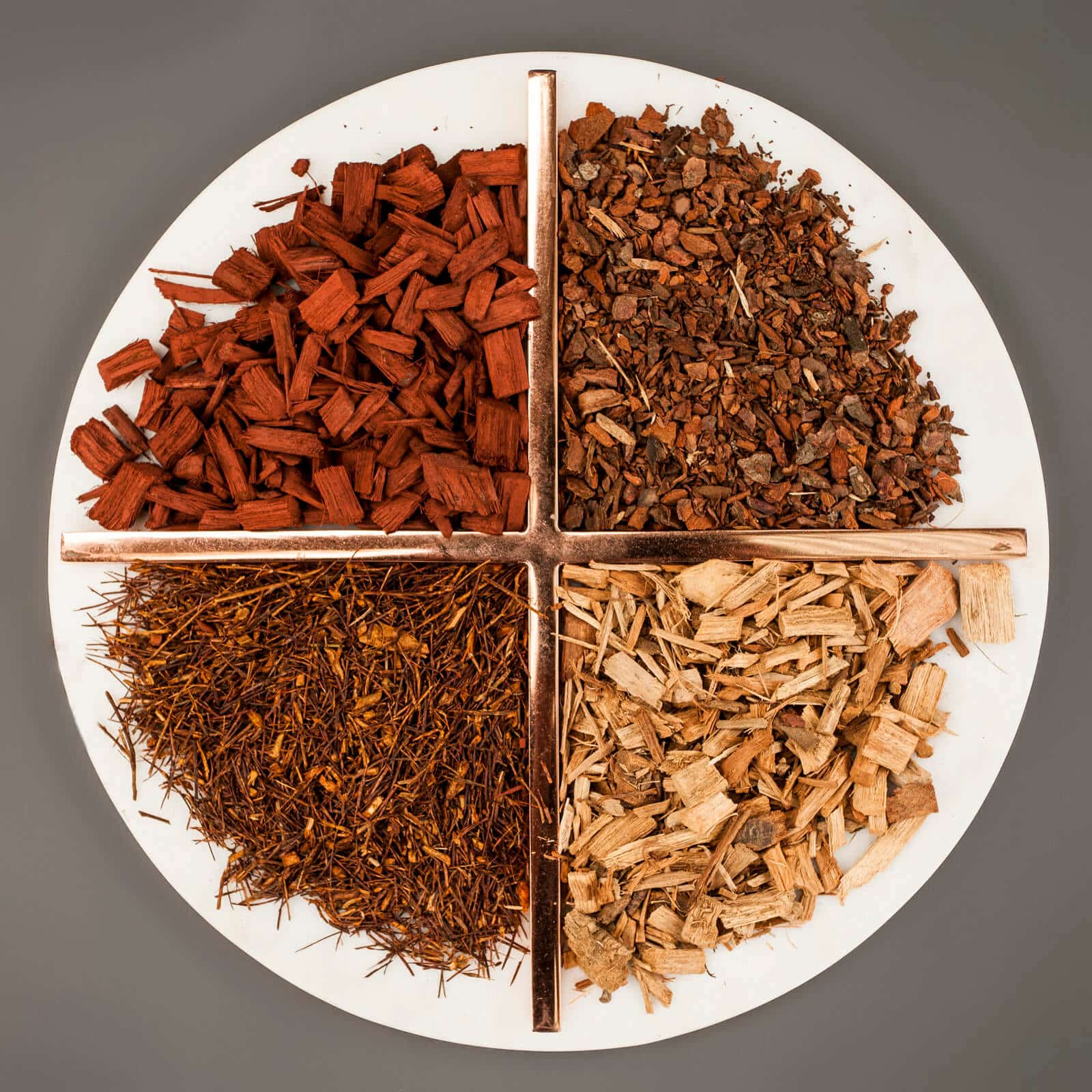 Four distinct piles of wood chips of varying shades on a circular white plate.