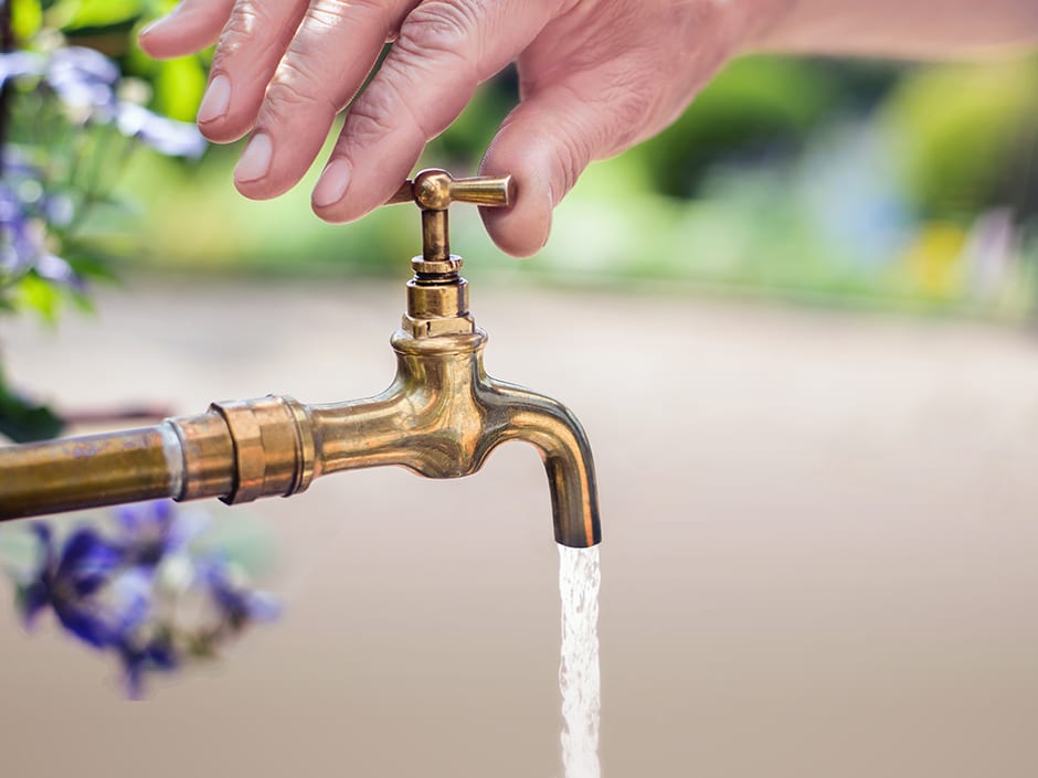 A person's hand holding the head of a golden-coloured tap, from which water is running.