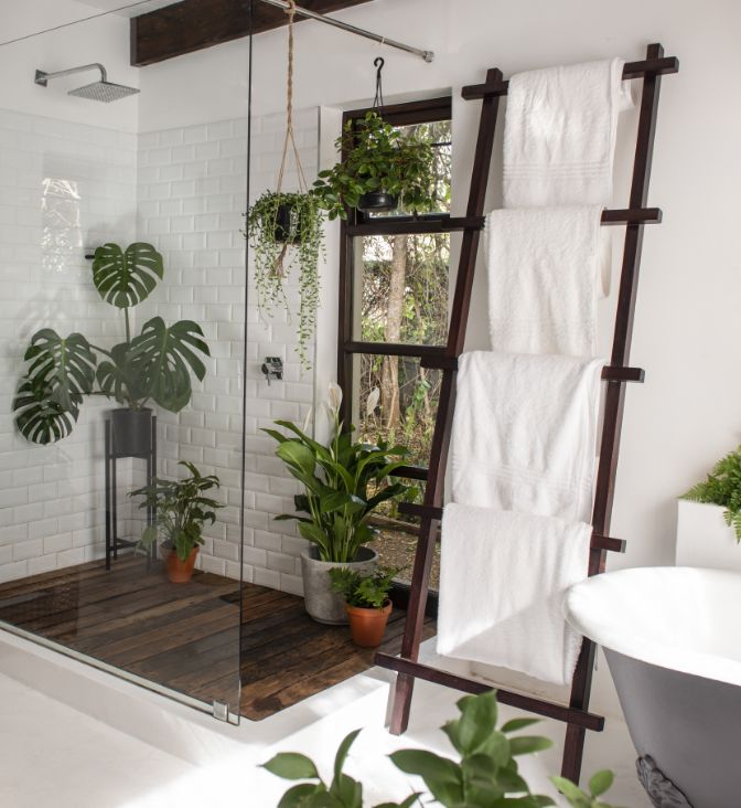 Indoor plants including monstera and hanging planters in a white room with subway tile walls.