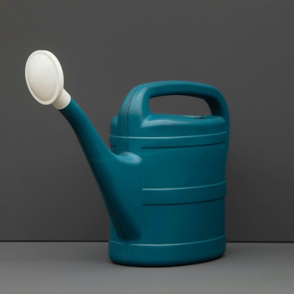 A dark blue-green watering can with white spout against a dark background.