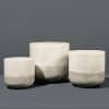 Three white ceramic planters of varying sizes with subtle striped textures, sat on a grey background.