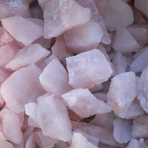 A close-up of a pile of rough rose quartz rocks, each with a light pink hue.