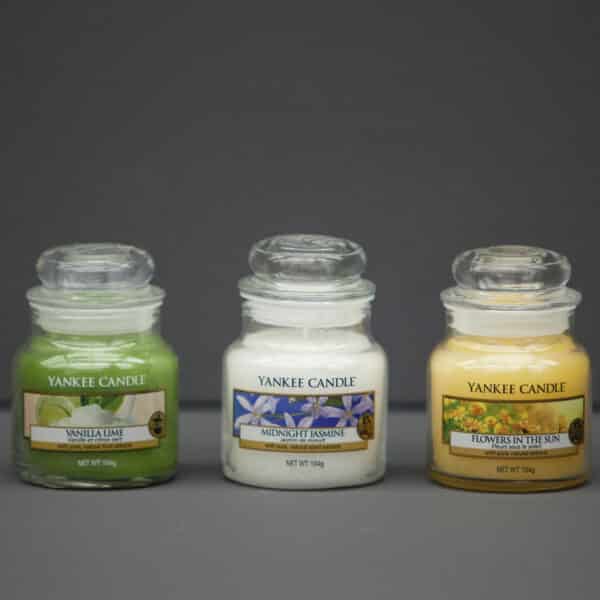 Three glass jars of Yankee Candle scented candles in Vanilla Lime, Midnight Jasmine, and Flowers in the Sun fragrances.
