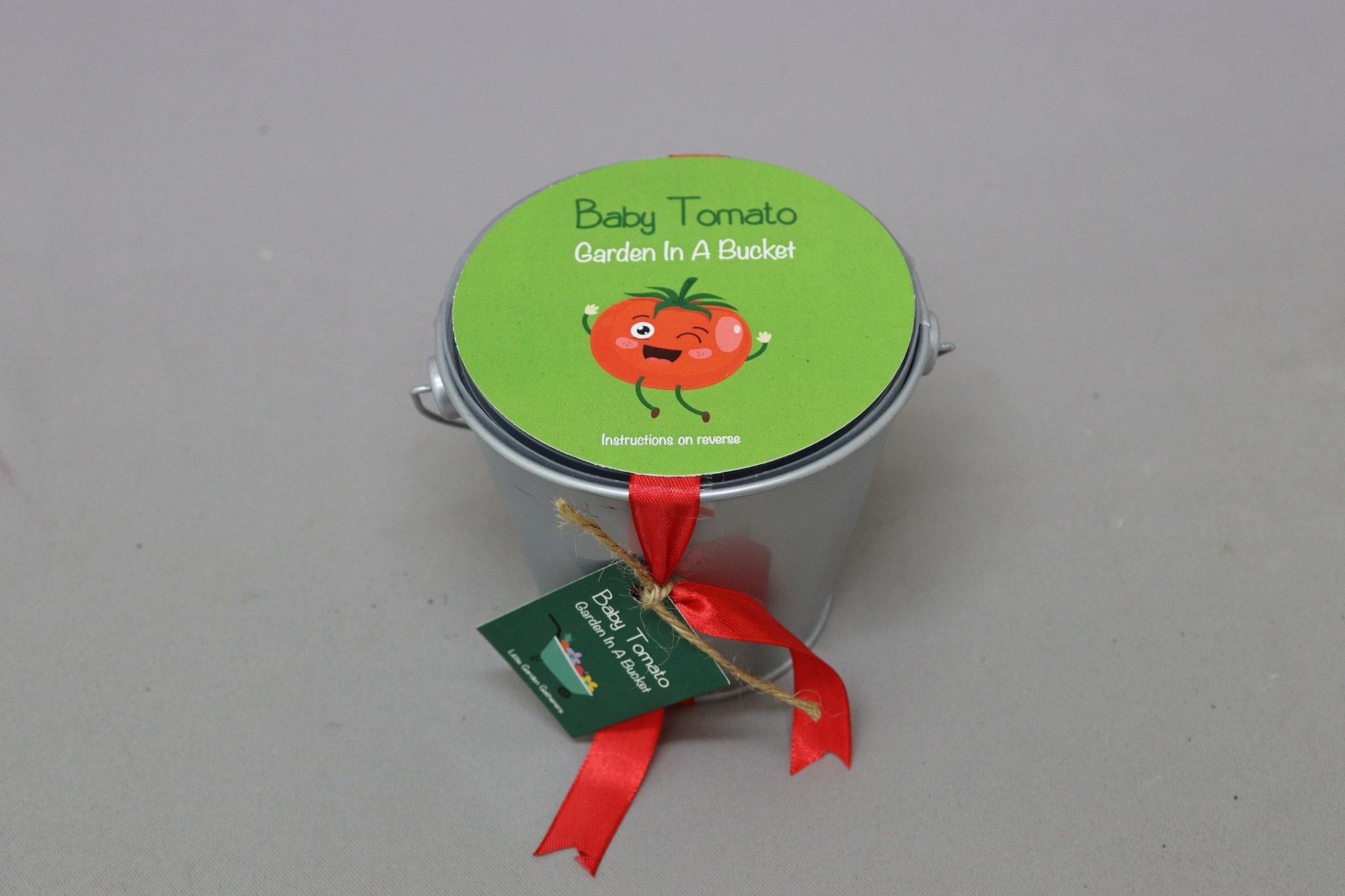 Small silver bucket with branded green lid containing seeds and soil to grow tomatoes.