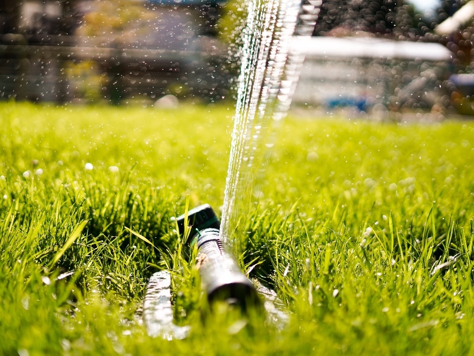 Lawn sprinkler spraying water across a lush green lawn on a sunny day.